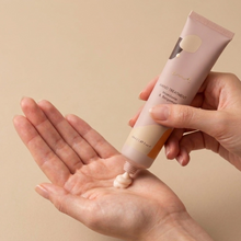 Load image into Gallery viewer, Hand applying hand treatment cream from a tube on a beige background