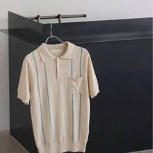 Load image into Gallery viewer, Beige polo shirt with green stripes on a hanger against a black and white background