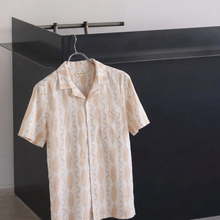 Load image into Gallery viewer, Beige patterned shirt on a hanger against a black and white geometric background