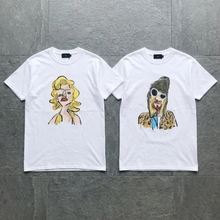 Load image into Gallery viewer, Two white t-shirts with artistic portraits on a gray surface