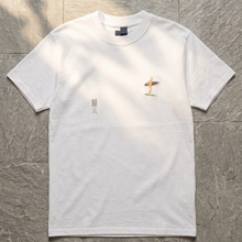 Load image into Gallery viewer, White t-shirt with a small graphic on a textured gray surface