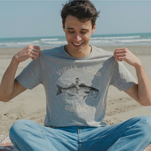 Load image into Gallery viewer, Man sitting on a beach wearing a t-shirt with a graphic design.