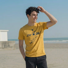 Load image into Gallery viewer, Person wearing a yellow t-shirt with 'Stay Cool' text on a beach