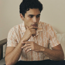 Load image into Gallery viewer, Man sitting on a couch with his hand on his chin, wearing a patterned shirt.
