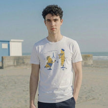 Load image into Gallery viewer, Man wearing a white t-shirt with a graphic design on a beach