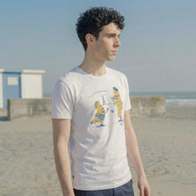 Load image into Gallery viewer, Person wearing a white t-shirt with a graphic design on a beach