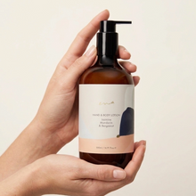 Load image into Gallery viewer, Hand holding a bottle of hand and body lotion with a visible label on a beige background