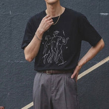 Load image into Gallery viewer, Person wearing a black t-shirt with a graphic design against a dark wall.