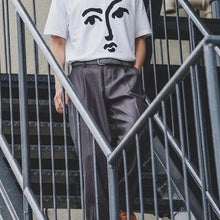 Load image into Gallery viewer, Person wearing a white t-shirt with a face design and gray pants on a staircase.