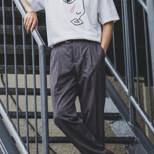 Load image into Gallery viewer, Person wearing a white t-shirt with a face design and gray pants, standing on metal stairs.