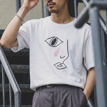 Load image into Gallery viewer, Man wearing a white t-shirt with a graphic design, standing outdoors.