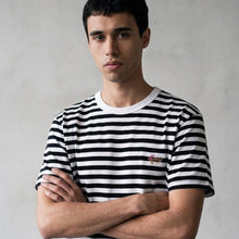 Load image into Gallery viewer, Man wearing a black and white striped shirt with a brand logo, standing against a plain background