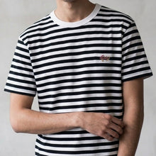 Load image into Gallery viewer, Person wearing a black and white striped t-shirt with a small logo on a plain background