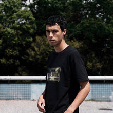 Load image into Gallery viewer, Person wearing a black t-shirt with a graphic design outdoors