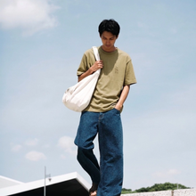 Load image into Gallery viewer, Man holding a white bag against a clear blue sky