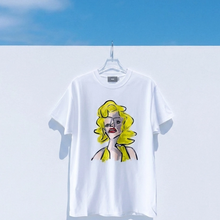 Load image into Gallery viewer, White t-shirt with a graphic design of a woman with yellow hair on a hanger against a blue sky.