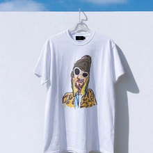 Load image into Gallery viewer, White t-shirt with a graphic design of a person in sunglasses and a leopard print jacket, hanging against a blue sky.