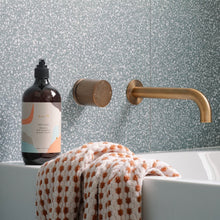 Load image into Gallery viewer, Bottle of soap on a bathtub with gold faucet and towel against a patterned wall
