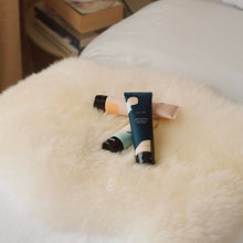 Load image into Gallery viewer, Two cosmetic tubes on a fluffy white surface with books in the background