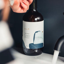 Load image into Gallery viewer, Bottle of wine with a label held by a hand against a dark background