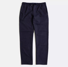 Load image into Gallery viewer, A pair of blue pleated trousers with small pleats to the front waist area, featuring two side seam pockets, two welt pockets on the rear, corozo buttons, and a zip fly opening. The trousers have subtle orange internal piping.