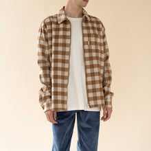 Load image into Gallery viewer, Person wearing a brown and beige checkered shirt over a white t-shirt with blue pants on a beige background