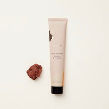 Load image into Gallery viewer, A tube of hand treatment cream with a beige label, next to a small brown rock, on a white background.