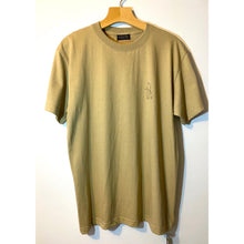 Load image into Gallery viewer, An almond-colored, short-sleeved crewneck t-shirt displayed on a hanger, with a small round logo embroidered near the neckline.