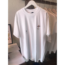 Load image into Gallery viewer, A white crew neck t-shirt with short sleeves, displayed on a hanger. The t-shirt features "surf" graphic design on the front.